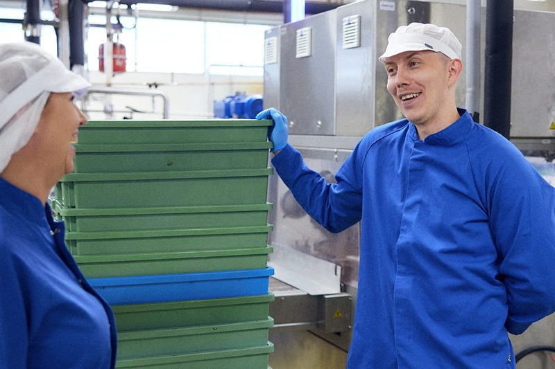 Kaksi elintarviketeollisuuden työntekijää siirtää laatikoita tuotantotiloissa.